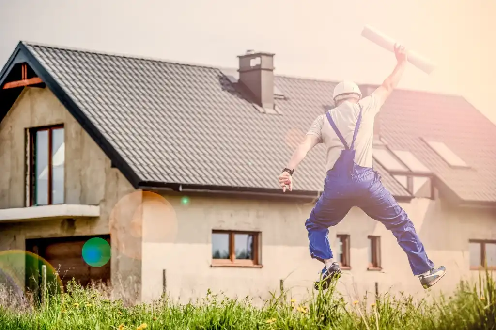 Man in hard hat holding building plans celebrating in front of home under construction