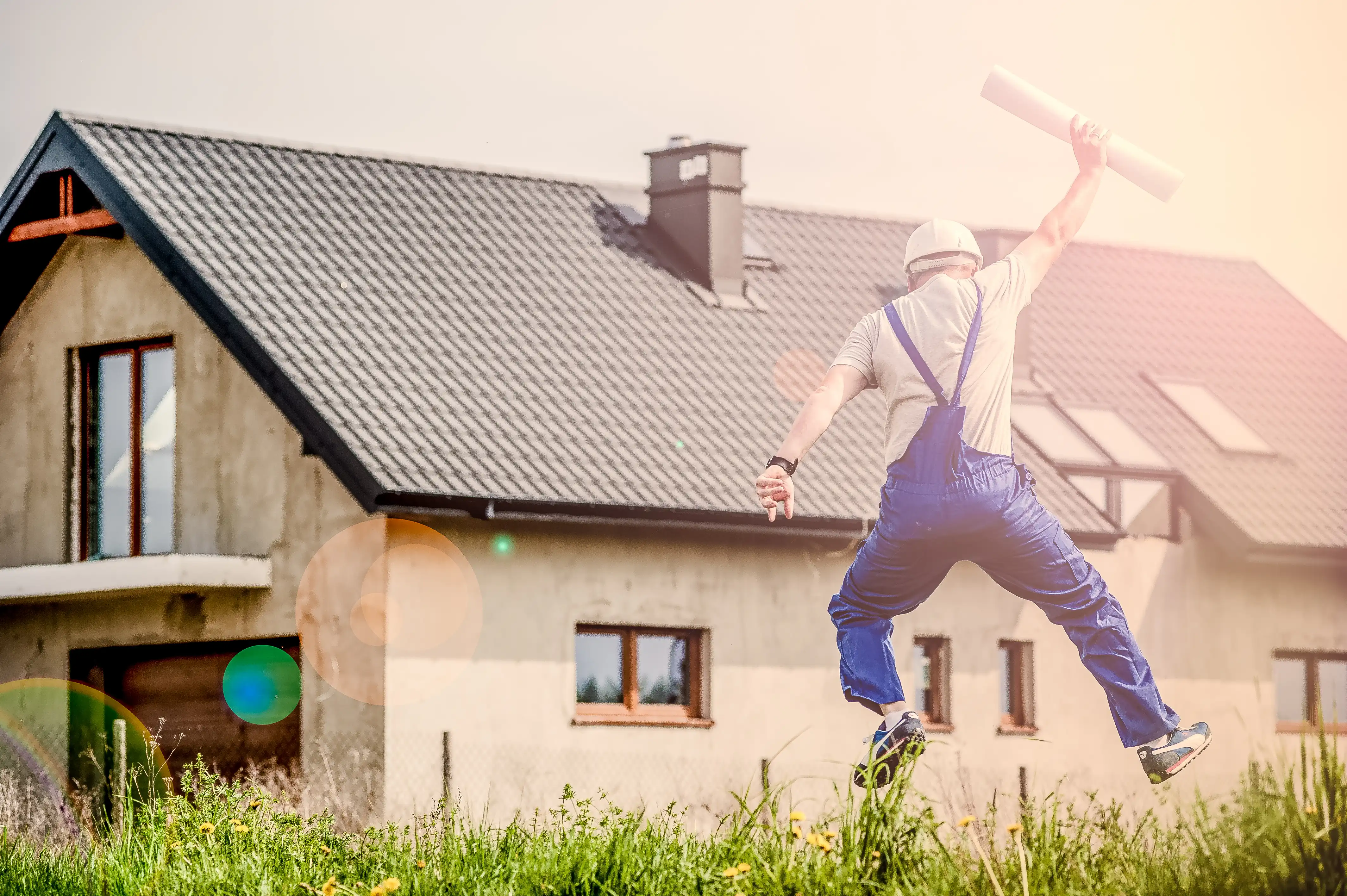 Man in hard hat holding building plans celebrating in front of home under construction