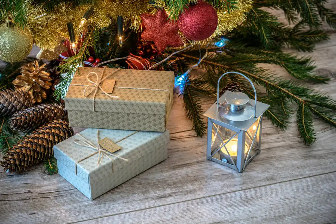 Christmas tree with wrapped presents underneath, pine cones, and a lamp creating a cozy holiday setting