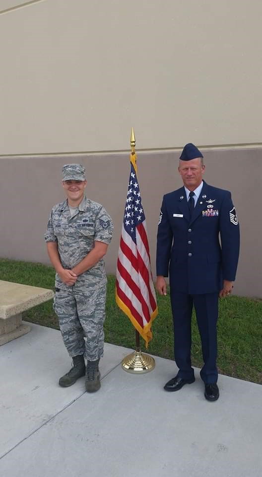 Veteran Scott Dunn and his son in military uniforms standing beside an American flag