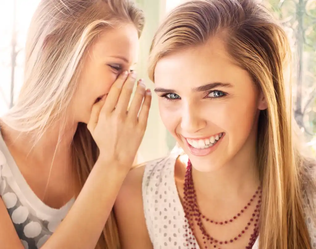 Two women talking with one whispering a secret to the other, representing homebuying tips and insider advice