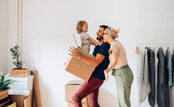 Happy first-time homebuyer family moving into their new home, smiling and carrying boxes.
