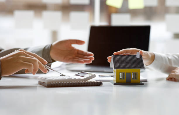 Hands discussing mortgage refinance options with a calculator, notebook, and a model house on the table, symbolizing home equity and loan refinancing solutions.